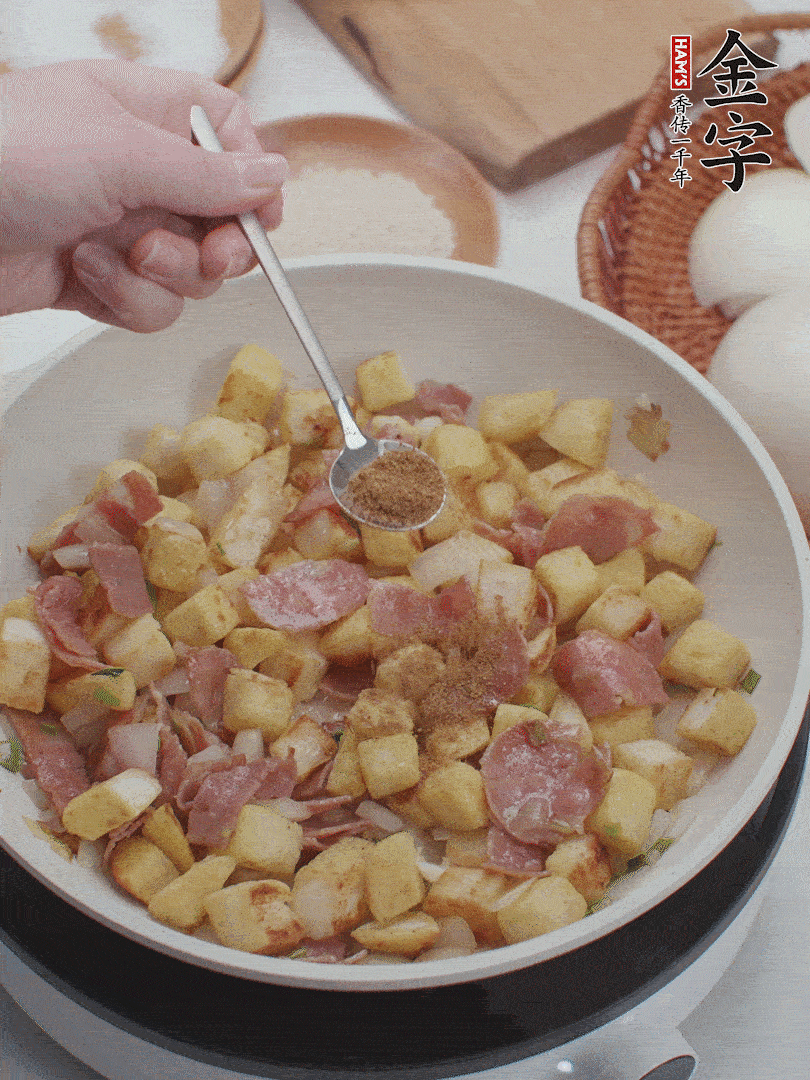 起鍋少油，煸香洋蔥丁、蔥白，加入金字培根火腿翻炒幾下，再加入饅頭丁、1小勺孜然粉、少許鹽翻炒均勻并鋪平。